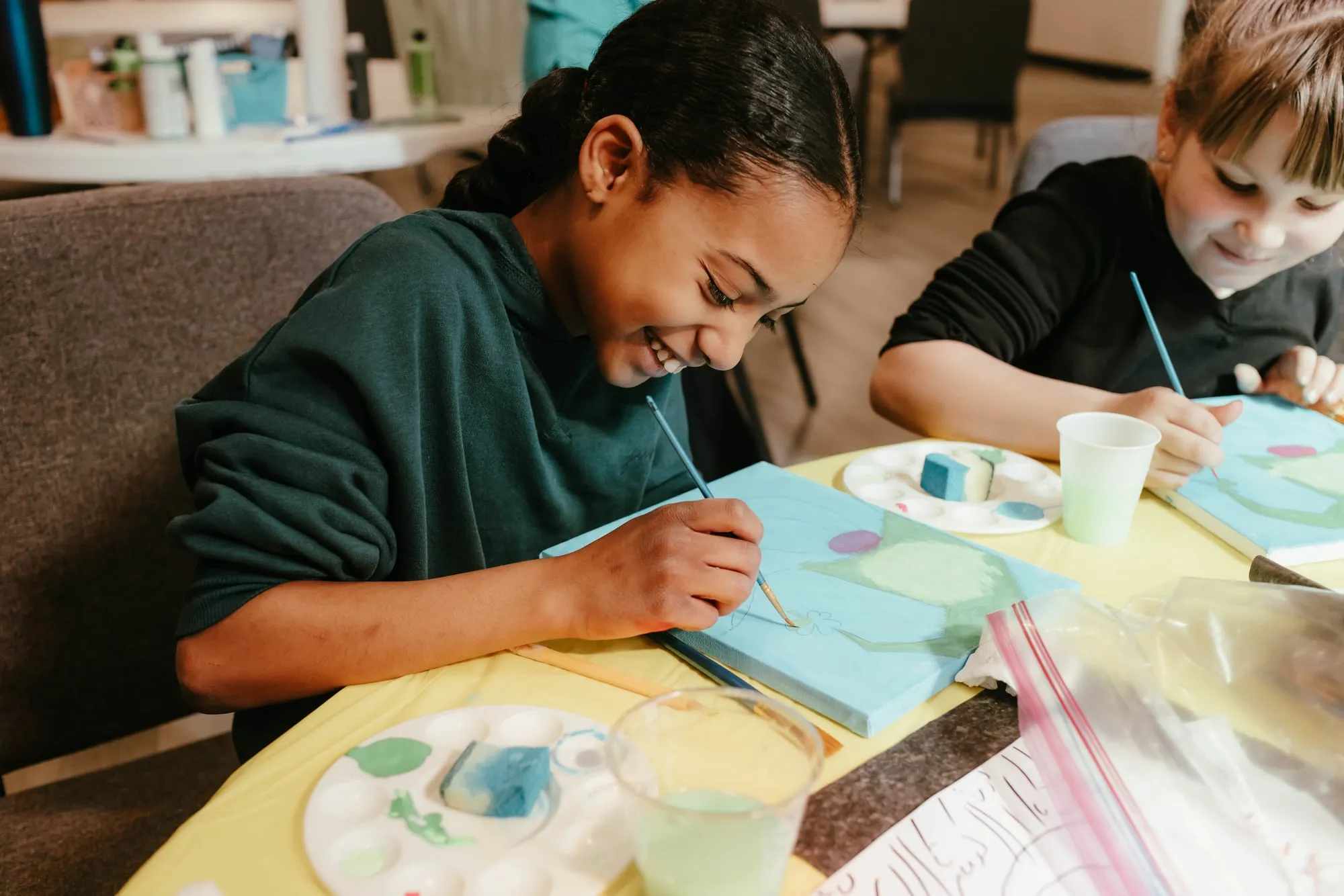 Two students smiling while painting at a classroom table